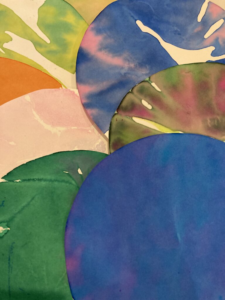 Colorful, circular paper cutouts overlap, featuring vibrant hues like blue, green, orange, and pink. This artwork showcases creative use of color and shape.