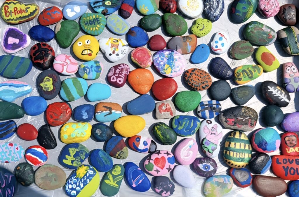Colorfully painted rocks display various designs and messages, showcasing creativity and community expression in an art installation.