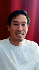 Smiling man in a white shirt against a red background. The warm expression suggests a friendly and approachable demeanor, enhancing the page's welcoming tone.